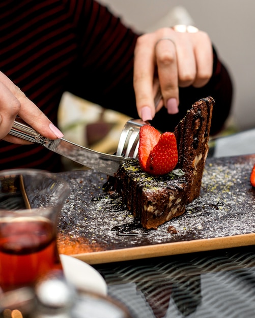 De vrouw eet chocoladecake met aardbeiplakken op de bovenkant