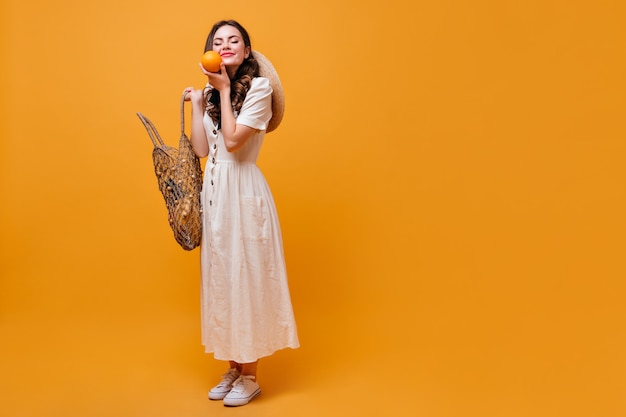 De vrouw houdt koordzak en sinaasappel vast. Brunette meisje schattige glimlach op een oranje achtergrond.