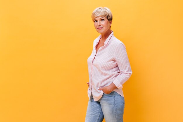 De vrouw in jeans en overhemd stelt op oranje achtergrond