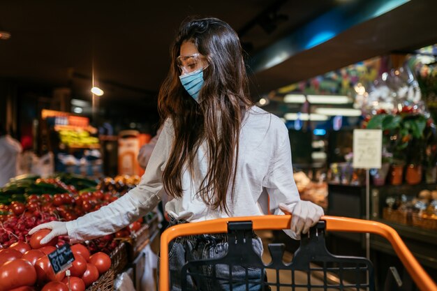 De vrouw met een chirurgisch masker gaat tomaten kopen.