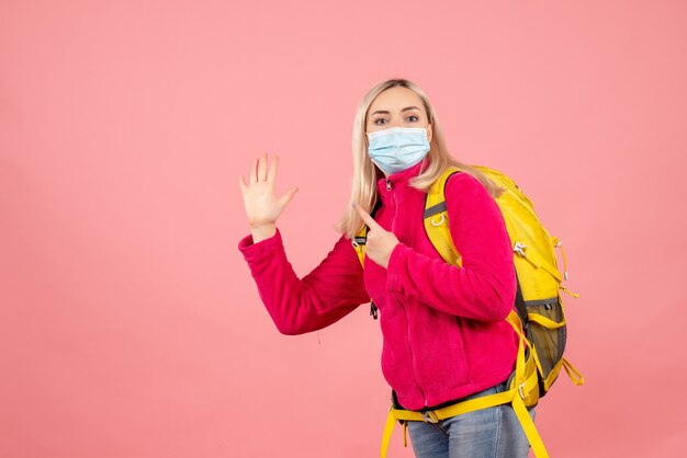 De vrouw van de vooraanzichtreiziger met gele rugzak die masker draagt dat high five geeft