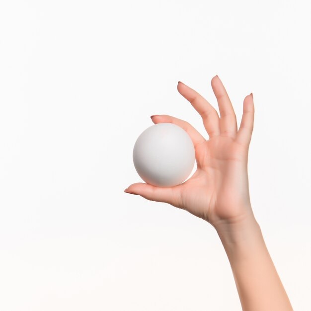 De vrouwelijke hand die witte lege piepschuimbal houdt tegen het wit.
