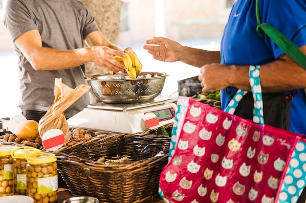 Gratis foto de zak van de mensenholding het kopen bananen van fruitverkoper in markt