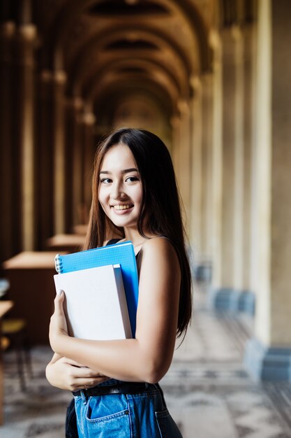 De zekere Aziatische boeken van de studentenholding en het glimlachen bij camera, onderwijs, campus, vriendschap en mensenconcept