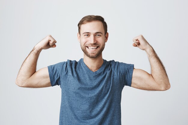 De zekere glimlachende mens opleiding in gymnastiek, buigt sterke bicepsen, toont spieren