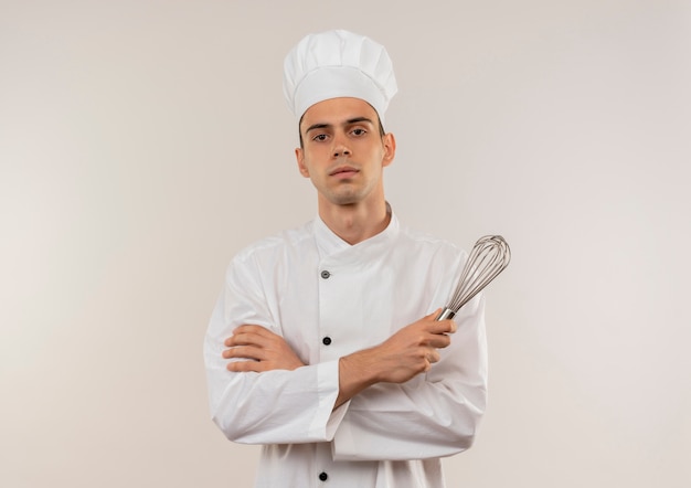 De zekere jonge mannelijke kok die de holding van de chef-kok eenvormige kruising draagt, zwaait op geïsoleerde witte muur met exemplaarruimte