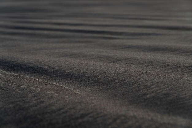 De zwarte macrofotografie van het zandstrand. Zijdeachtige zwarte strandtextuur met ondiepe diepte van gebied. Minimalistische zwarte achtergrond. Voulcanic zandkust van Tenerife.