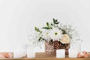 Gratis foto decoratieve bloemenvaas met witte kaarsen op houten tafel tegen witte achtergrond