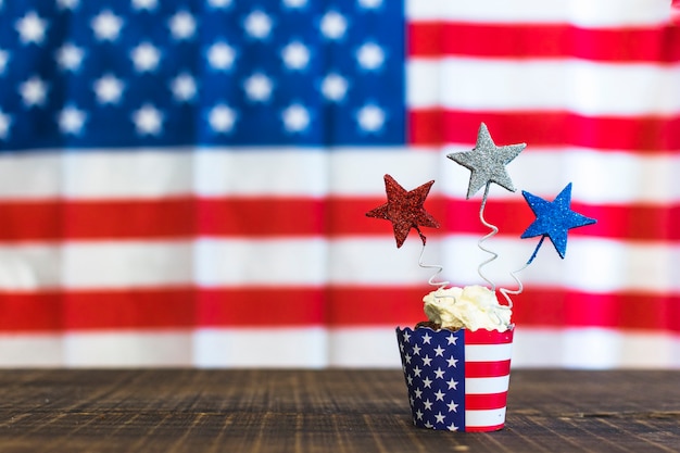 Decoratieve cupcakes met rood; zilveren en blauwe sterren op houten bureau tegen Amerikaanse vlaggen voor 4 juli