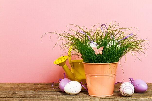 Decoratieve Kleurrijke Eieren In Bloempot Met Vers Groen Gras Op Houten Tafel Op Roze Achtergrond. Horizontaal met kopieerruimte.