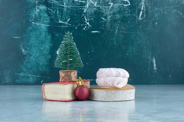 Decoratieve opstelling van een kerstbal, een boomfiguur op een boekje en gestapelde koekjes op marmer.