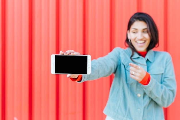 Defocused glimlachende vrouw die celtelefoon toont