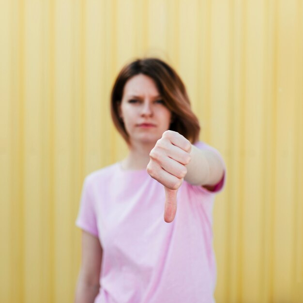 Defocused jonge vrouw die duim neer tegen gele achtergrond toont