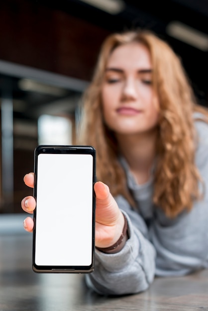 Gratis foto defocused jonge vrouw die slimme telefoon op hardhoutvloer houdt