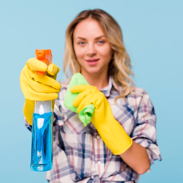 Defocused schonere vrouwen bespuitende detergent fles met holdingsservet in haar hand tegen blauwe achtergrond