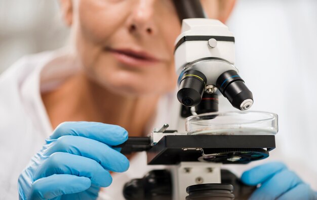 Defocused vrouwelijke wetenschapper die door microscoop kijkt