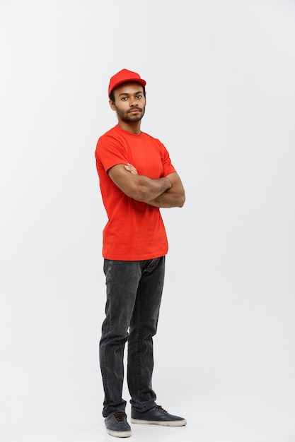 Delivery Concept - Knappe Afro-Amerikaanse leverancier man gekruiste armen over geïsoleerd op grijze studio achtergrond. Ruimte kopiëren.