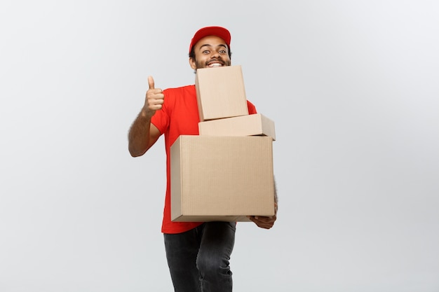 Delivery Concept - Portret van gelukkige Afro-Amerikaanse leveringsman in rode doek met een doospakket. Geïsoleerd op grijze studio achtergrond. Ruimte kopiëren.