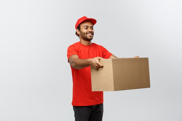 Delivery Concept - Portret van gelukkige Afro-Amerikaanse leveringsman in rode doek met een doospakket. Geïsoleerd op grijze studio achtergrond. Ruimte kopiëren.