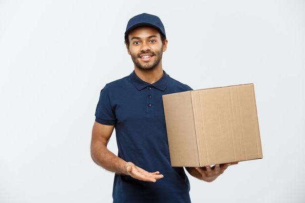 Delivery concept - portret van gelukkige afro-amerikaanse leveringsman in rode doek met een doospakket. geïsoleerd op grijze studio achtergrond. ruimte kopiëren.