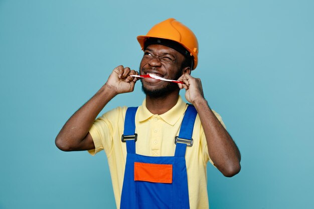 Denken brengen duct tape in de mond jonge Afro-Amerikaanse bouwer in uniform geïsoleerd op blauwe achtergrond