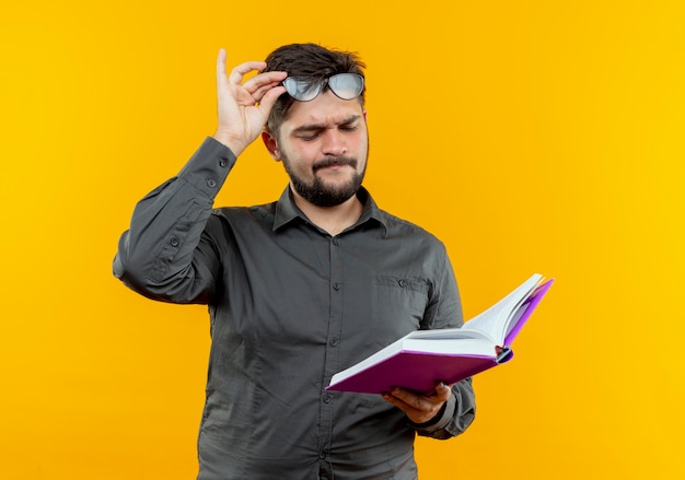 Denken jonge zakenman bril houden en kijken naar boek op geel