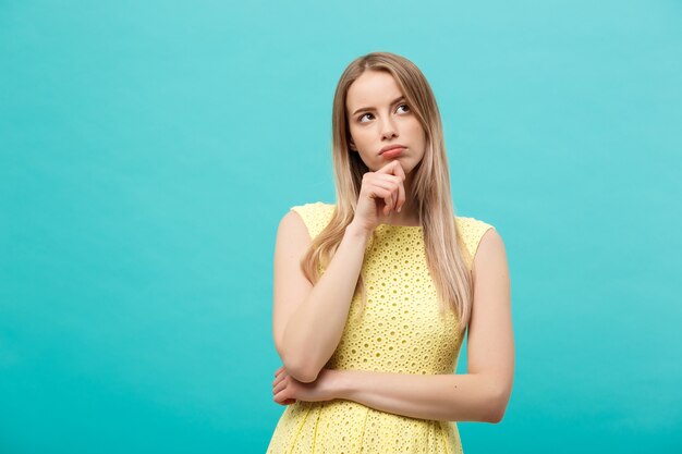 Denken jonge zelfverzekerde vrouw in gele jurk opzoeken geïsoleerd op blauwe achtergrond