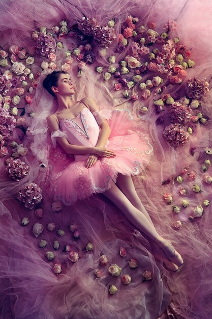 Denkend aan warm. Bovenaanzicht van mooie jonge vrouw in roze ballet tutu omgeven door bloemen. Lentestemming en tederheid in koraallicht. Kunst foto. Concept van de lente, bloesem en het ontwaken van de natuur.