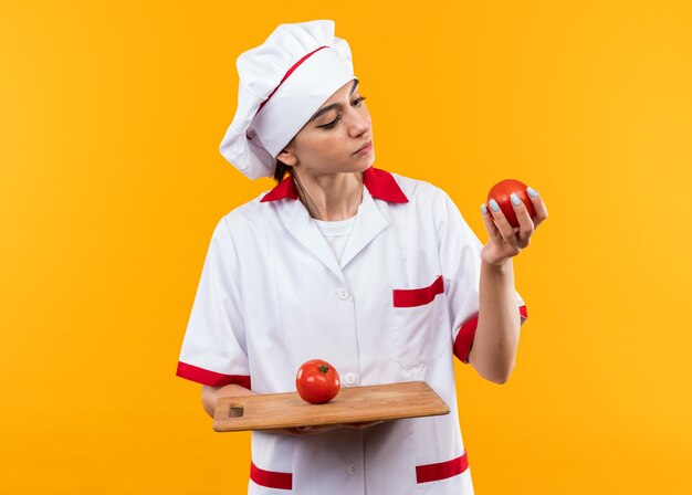 Denkend jong mooi meisje in chef-kok uniform houden en kijken naar tomaten op snijplank