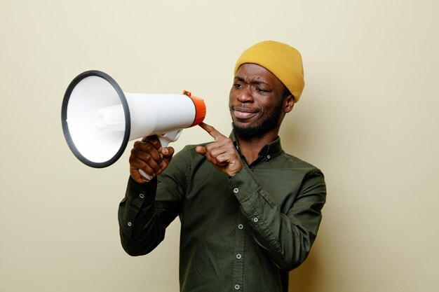 denkende jonge afro-amerikaanse man in hoed met een groen shirt, vasthoudend en kijkend naar luidspreker geïsoleerd op een witte achtergrond