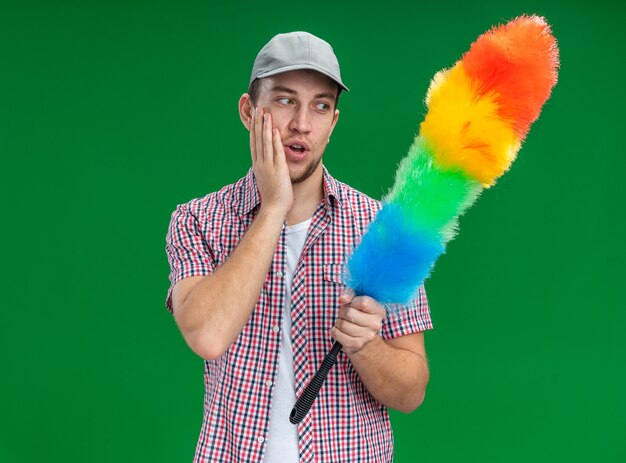 denkende jonge kerel die een dop draagt en kijkt naar pipidaster geïsoleerd op een groene muur