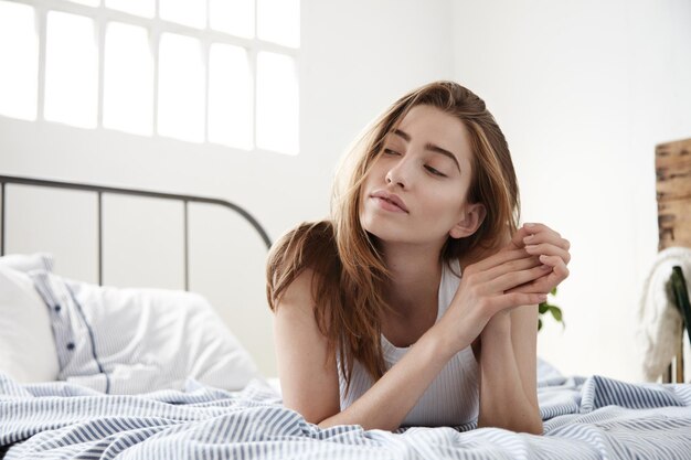 Denkende vrouw die opzij kijkt, ligt in het bed in een lichte witte loft