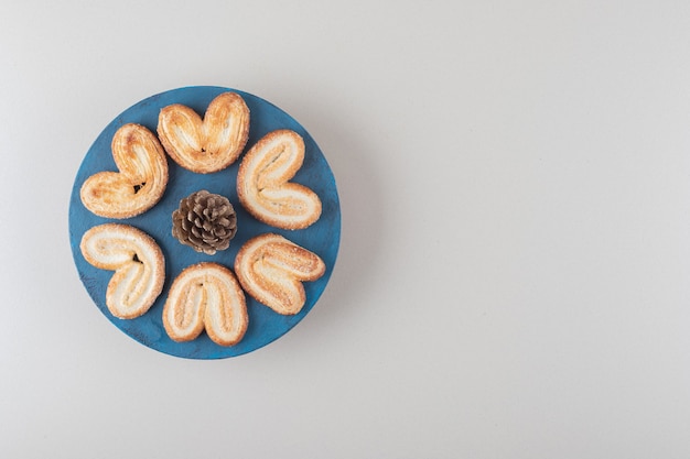 Gratis foto dennenappel omgeven door schilferige koekjes op een schotel op marmeren achtergrond.