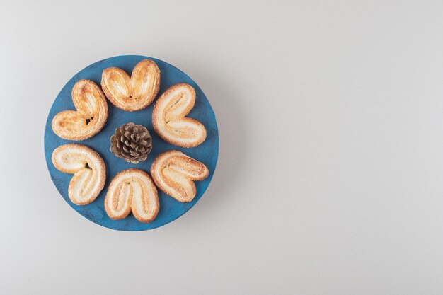 Dennenappel omgeven door schilferige koekjes op een schotel op marmeren achtergrond.