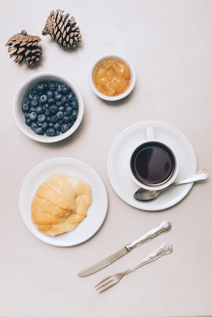 Dennenappels; bosbessen; jam; brood en koffiekop op witte achtergrond