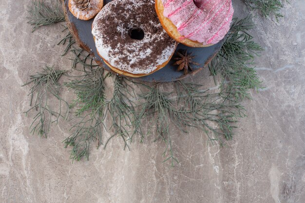 Dennenbladeren onder een bord met donuts op marmer.