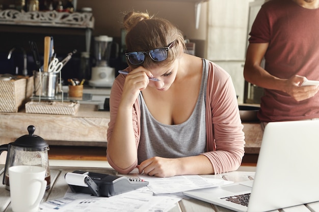 Depressief paar geconfronteerd met kredietprobleem. Beklemtoonde vrouw die uitgeput kijkt terwijl thuis het doen van rekeningen, hard het proberen om familiekosten te drukken, pen houdt en noodzakelijke berekeningen op calculator maakt