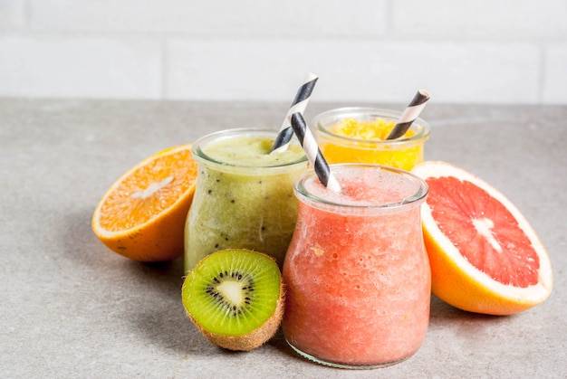 Detox biologische dieetdranken, zelfgemaakte tropische smoothies - kiwi, sinaasappel, grapefruit, in geportioneerde potten, met ingrediënten, op een grijze stenen tafel. copyspace