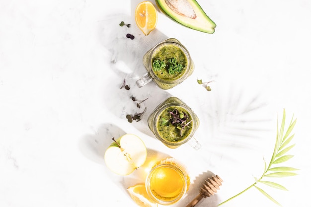 Detox groene smoothie - avocado, microgroen, citroen en honing op een witte steen of betonnen ondergrond. Harde verlichting en schaduw. Selectieve aandacht, kopieer ruimte. Bovenaanzicht.