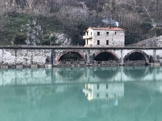 Devil Bridge omgeven door heuvels bedekt met groen en huizen die reflecteren op het water in Italië