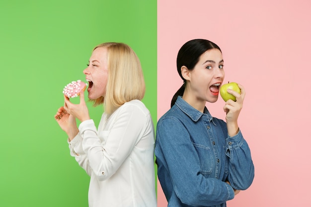 Dieet concept. Gezond, nuttig voedsel. Mooie jonge vrouwen die tussen fruit en ongezonde cake bij studio kiezen.