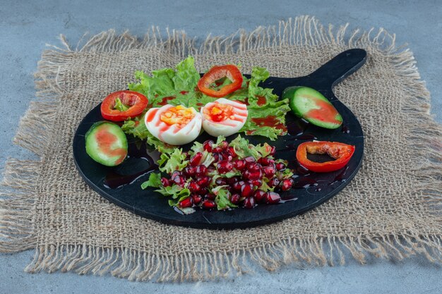 Dienblad met ontbijt gemaakt van gekookte eieren, plakjes komkommer en paprika en granaatappelsalade op marmer.