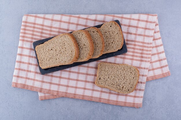 Dienblad van gesneden bruin brood op een gevouwen handdoek op marmeren oppervlak