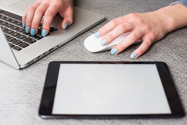 Digitale tablet dichtbij de hand van de onderneemster gebruikend laptop en muis op bureau