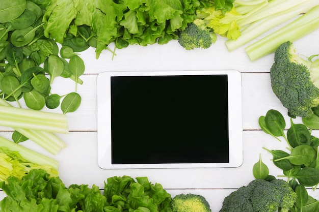 Digitale tablet die door groenten, gezond voedselconcept wordt omringd
