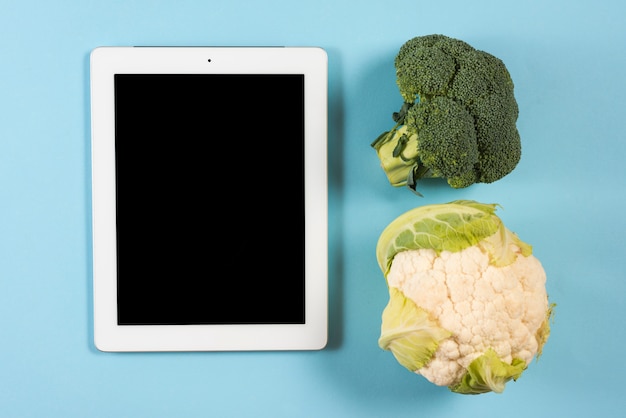 Gratis foto digitale tablet met broccoli en bloemkool op blauwe achtergrond