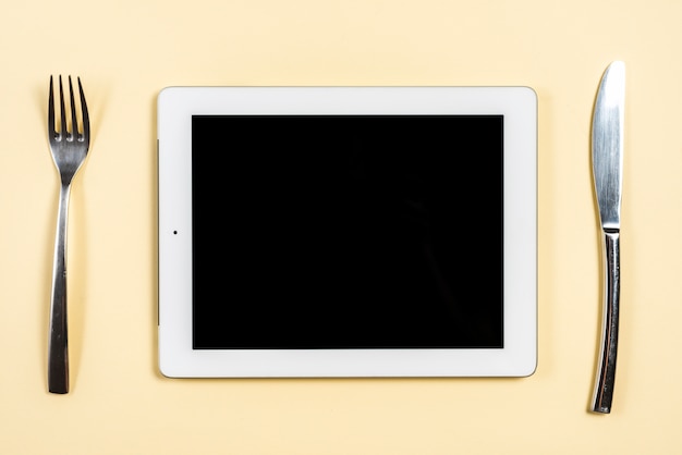Digitale tablet tussen de vork en butterknife op beige achtergrond