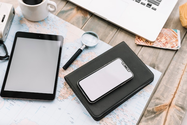 Digitale tablet; vergrootglas en dagboek op kaart over de houten tafel