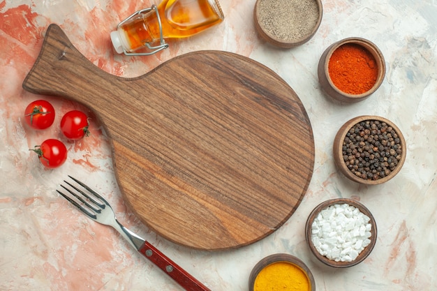 Diner achtergrond met tomaten op een witte plaat op houten snijplank en mes verschillende kruiden gevallen oliefles op gemengde kleur achtergrond