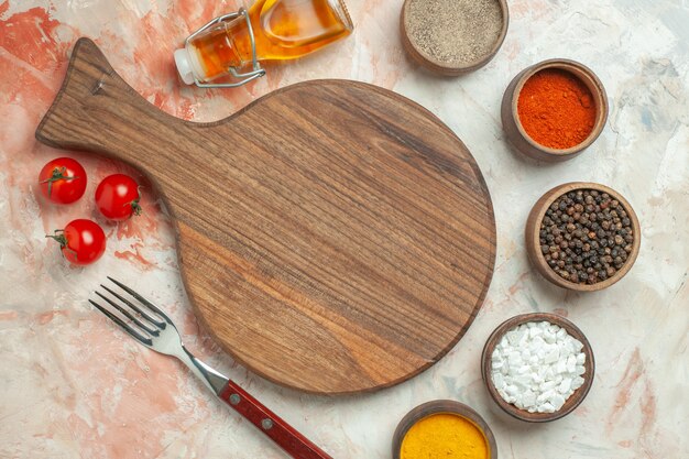 Diner achtergrond met tomaten op een witte plaat op houten snijplank en mes verschillende kruiden gevallen oliefles op gemengde kleur achtergrond
